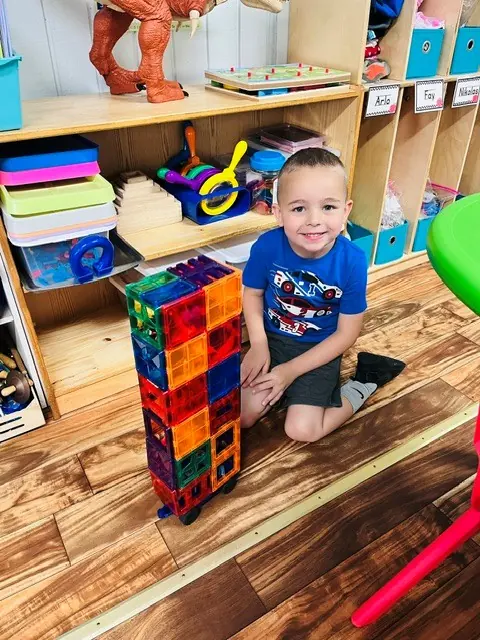 Child proudly standing beside a tall magnetic-tile structure